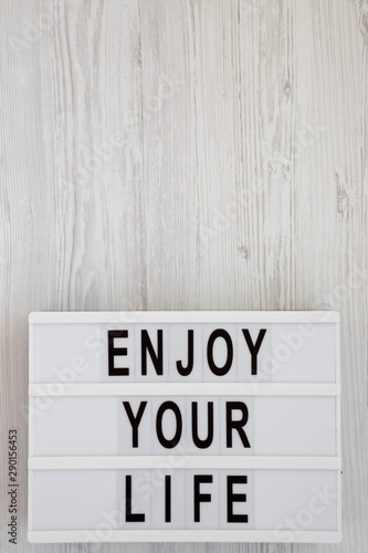 'Enjoy your life' words on a lightbox over white wooden surface, top view. Overhead, from above. Flat lay. Copy space.