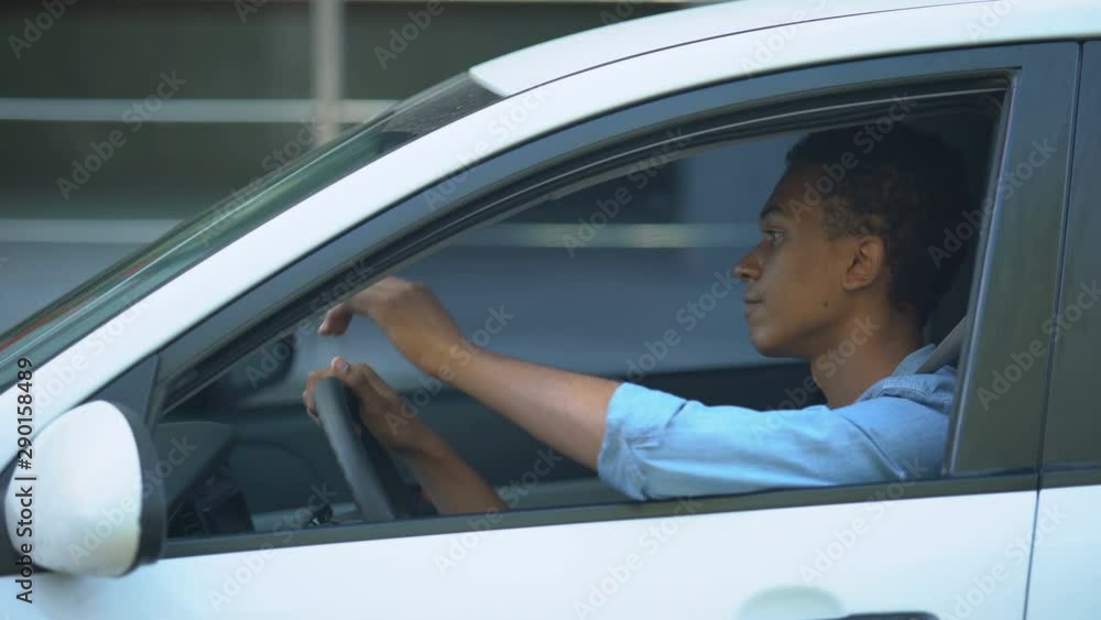 Tired mixed-race teenager stuck in traffic jam, leaning head on steering wheel Tired mixed-race teenager stuck in traffic jam, leaning head on steering wheel