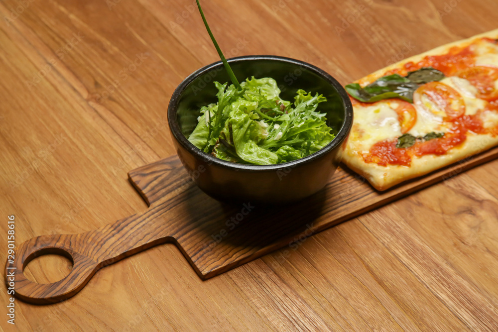 Homemade pizza served with a bowl of green salad on the wooden table Homemade pizza served with a bowl of green salad on the wooden table