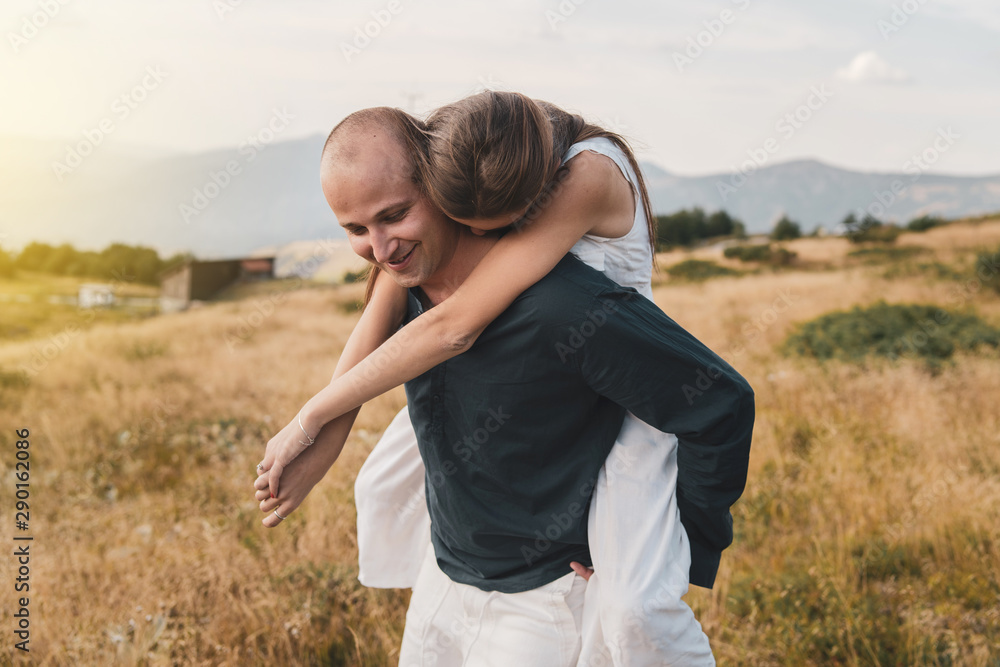 Young couple married in love man and woman young girl boyfriend husband is holding her on the mountain range in nature in summer or autumn day while she hug him from the back Young couple married in love man and woman young girl boyfriend husband is holding her on the mountain range in nature in summer or autumn day while she hug him from the back