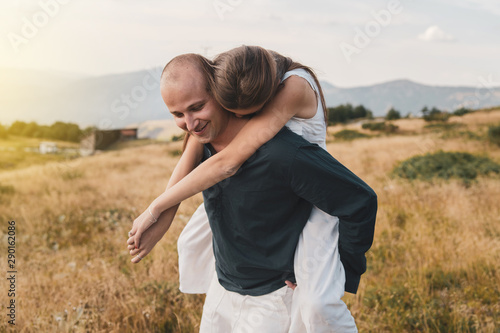 Young couple married in love man and woman young girl boyfriend husband is holding her on the mountain range in nature in summer or autumn day while she hug him from the back