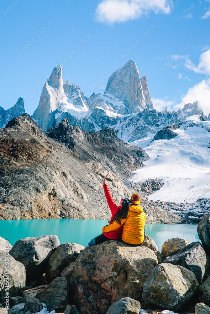 Couple in love on Mount Fitzroy, Patagonia trek. Scenic view of snowcapped mountain tops. Blue sky, turquoise lake and scenic rock landscape. Shot in Argentina. Nature, travel, adventure, hiking. - obrazy, fototapety, plakaty 