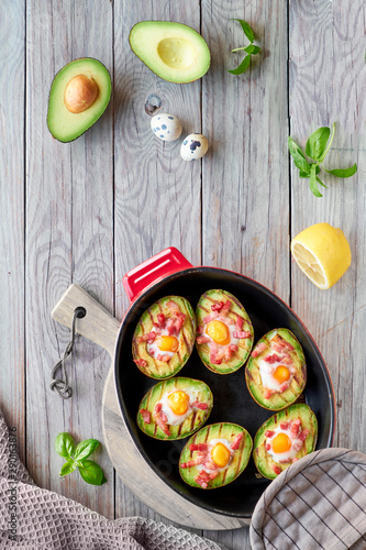 Top view on grilled avocado boats with bacon and quail eggs, flat lay on wood photo