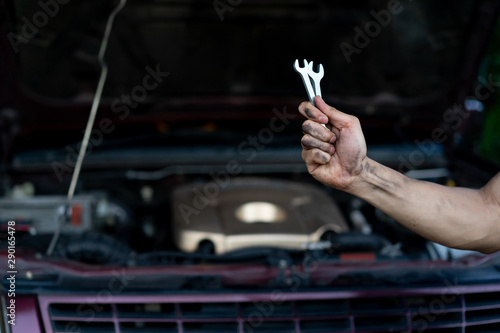 close up technician man hand holding two wrenches  over car's engine machinery background at garage repair shop for try to fixing problems , professional job concept photo