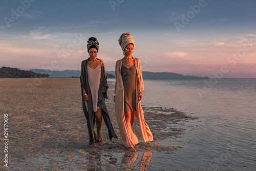 Photo two young beautiful girls in turban walking on the beach at sunset