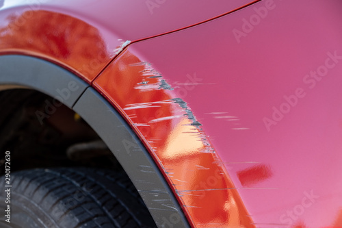 Closeup of deep scratches in red paint of car bumper