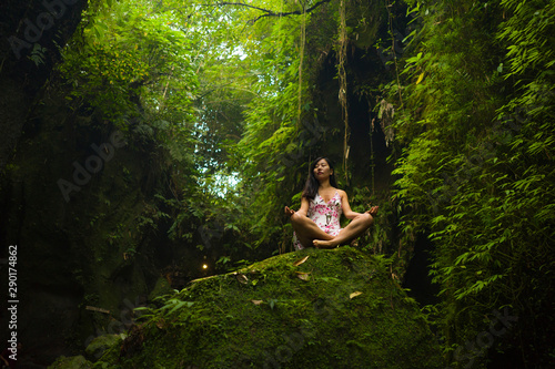 beautiful dreamy portrait of young attractive Asian woman enjoying nature sitting lotus pose doing yoga meditating relaxed at fresh and ethereal green forest feeling magical