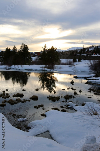 Colorado early spring nature background. Scenic landscape with covered by snow rocky mountains in sunlight during sunset and pond surrounded by snowy banks in a foreground during sunset. Keystone  CO