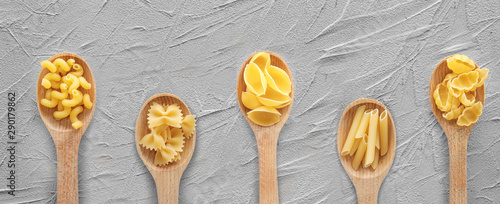 Wooden spoons with different uncooked pasta on grey table