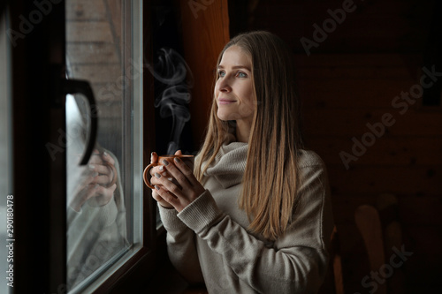 Young woman with hot drink near window on winter day