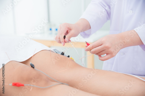 Close up of acupuncturist hands doing acupuncture with electrical stimulator at patient leg ,Alternative medicine concept.