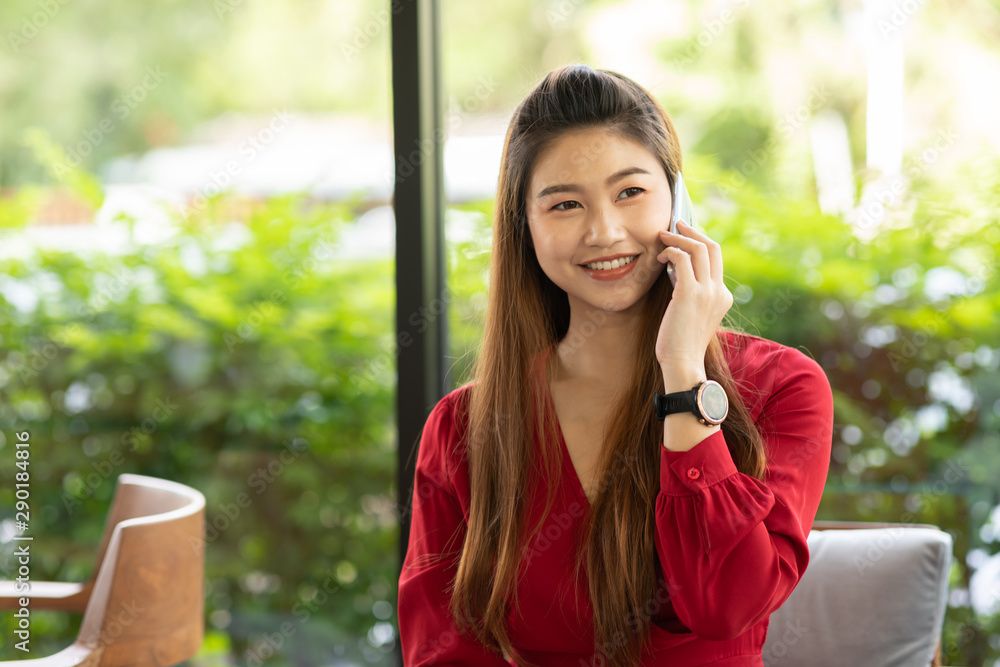 Business Asian woman wearing red dress working with laptop smile and talking with customer in smartphone get idea and requirement for success job outside office in coffee shop,Small Business Concept