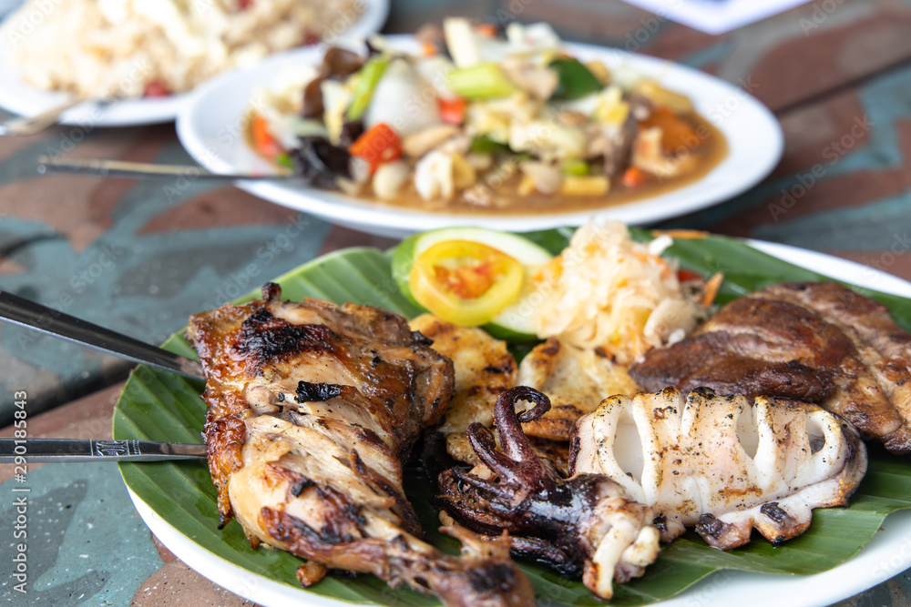 Pork, Squid, Chicken, Fish Filipino Barbecue on the Banana leaf plate Pork, Squid, Chicken, Fish Filipino Barbecue on the Banana leaf plate