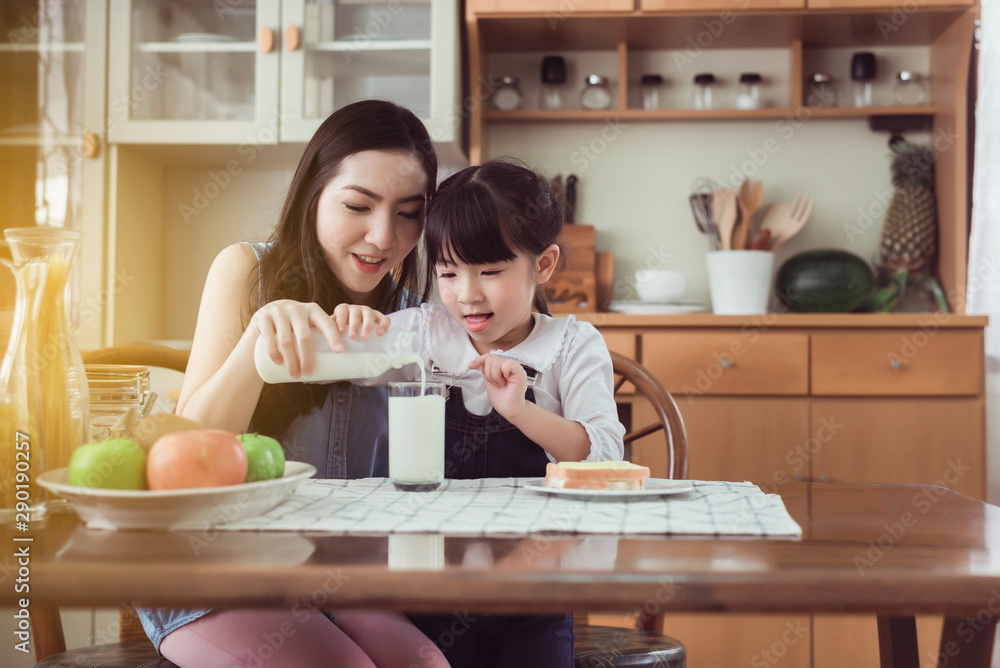 Asian single mother helping little daughter putting milk to glass with breakfast together at home kitchen in the morning Asian single mother helping little daughter putting milk to glass with breakfast together at home kitchen in the morning