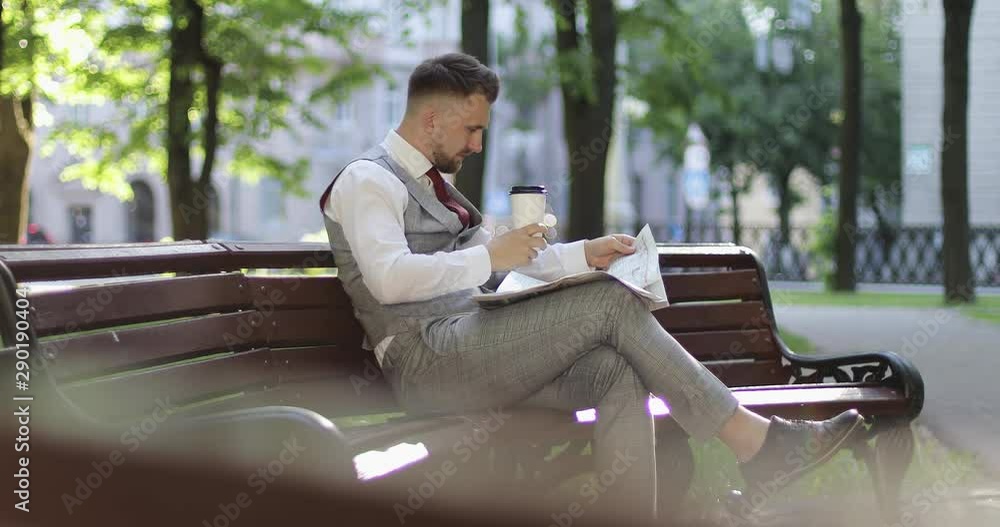 A businessman in an expensive suit is sitting on a park bench and reading a newspaper. A businessman in an expensive suit is sitting on a park bench and reading a newspaper.