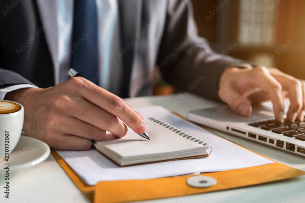Male businessman use a laptop computer and take notes in the notebook at the office desk in the morning. Male businessman use a laptop computer and take notes in the notebook at the office desk in the morning.