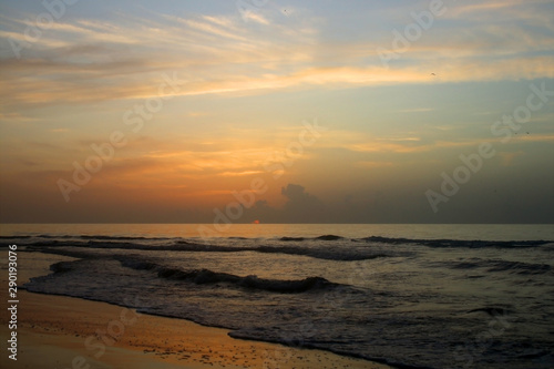 Early morning at the Atlantic beach. Marine background with rising sun and beautiful colorful sky reflects in a shallow water. Scenic seascape at the Pawleys Island, South Carolina, USA.