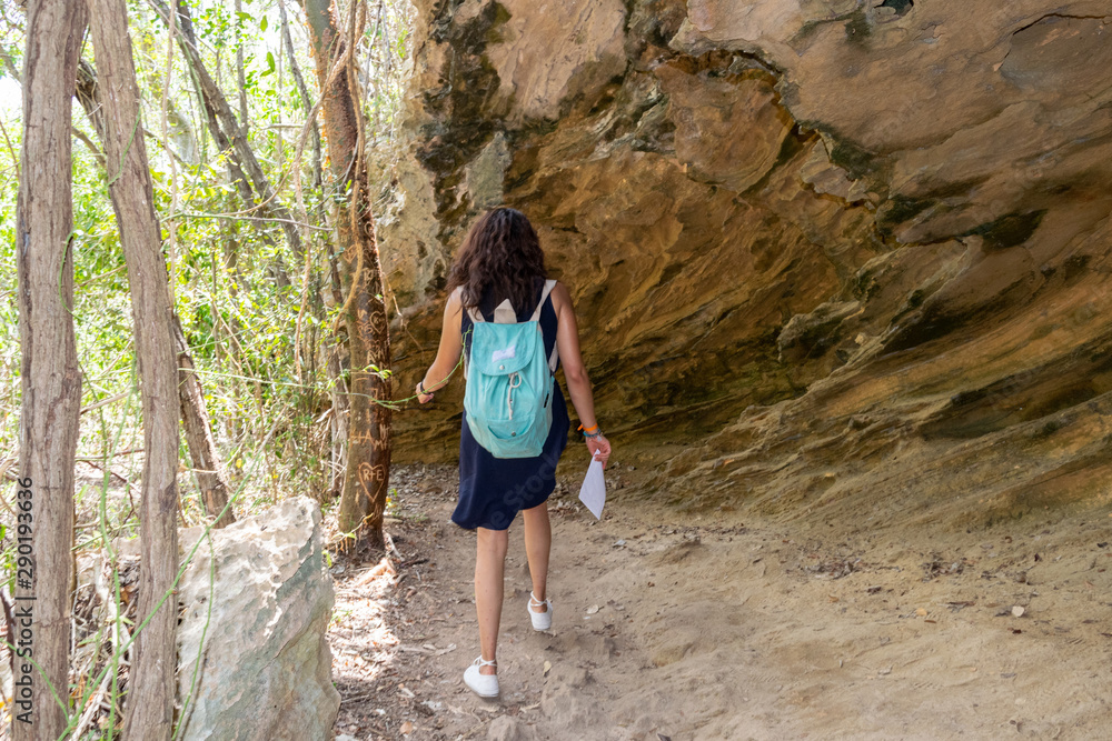 Naklejka premium Mujer caminando junto a cueva con un mapa en la mano