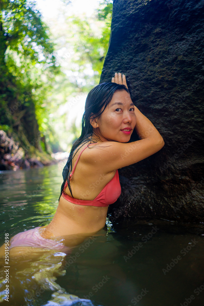 Fototapeta premium young beautiful happy Asian Chinese woman in bikini enjoying holidays at tropical forest refreshing relaxed in natural pool delighted by the tranquility at jungle lake