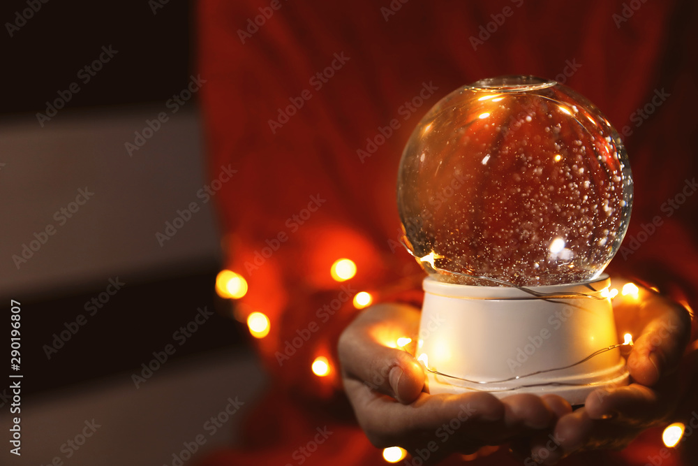 Woman holding snow globe and Christmas lights in darkness, closeup Woman holding snow globe and Christmas lights in darkness, closeup
