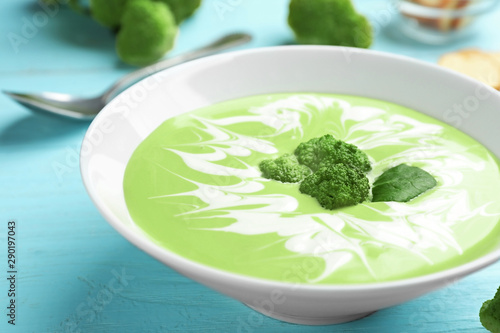 Bowl of cheese cream soup with broccoli served on blue wooden table, closeup