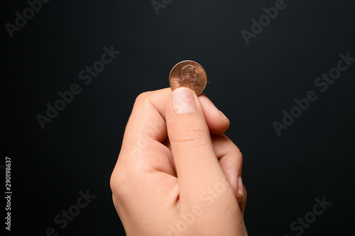 Young woman holding coin on black background, closeup view