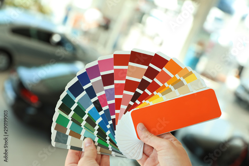 Young woman holding palette with color samples at car service station, closeup © New Africa