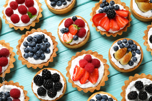 Many different berry tarts on blue wooden table, flat lay. Delicious pastries photo