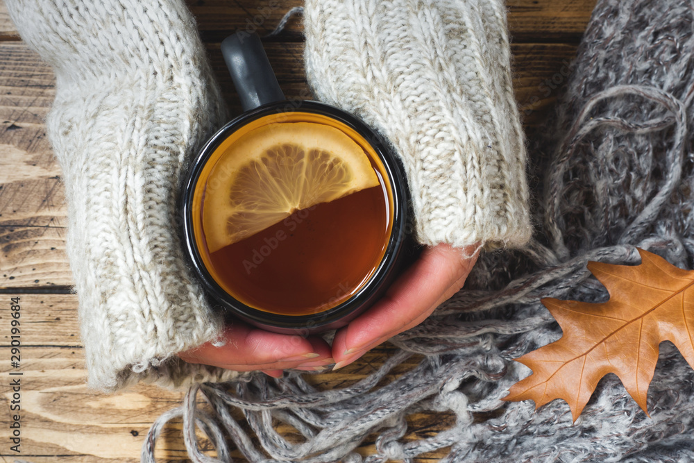 Woman's hand holding cup of tea with lemon on a cold day. Wooden table. Top view. Concept autumn Woman's hand holding cup of tea with lemon on a cold day. Wooden table. Top view. Concept autumn