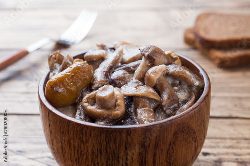 Stewed mushrooms in a sauce with sour cream and cheese in a wooden bowl.