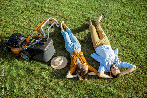 Beautiful man and woman resting on the grass near the lawn mower enjoying gardening on the backyard in the countryside