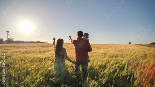 Young parents go with their son on a wheat field in the evening.