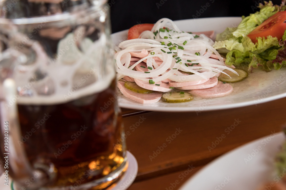 Naklejka premium Mann mit dunklen Bier und Bayrischen Wurstsalat aus Stadtwurst, Zwiebel Ringe, saure Gurken und Schnittlauch im Biergarten