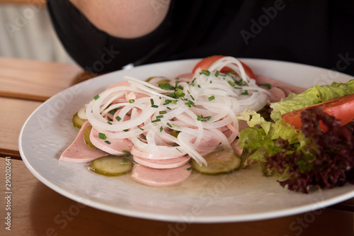 Mann isst Bayerischer Wurstsalat mit Stadtwurst, Zwiebel Ringe, saure Gurken und Schnittlauch im Biergarten photo