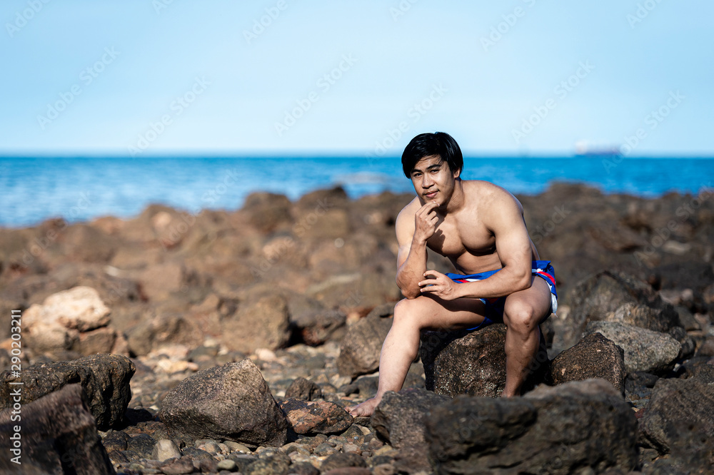 Bodybuilders are posing to show strength at the rocks by the sea.