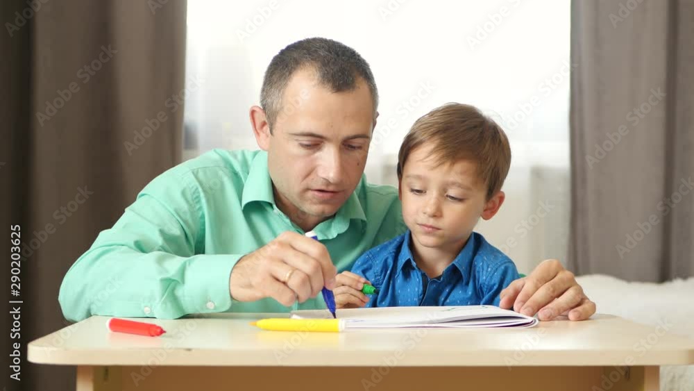 Happy family: dad and son spend time together. Father and son draw colored felt pen. Lifestyle, relationships, children's interests. Happy family: dad and son spend time together. Father and son draw colored felt pen. Lifestyle, relationships, children's interests.
