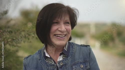 Portrait cloeup of happy beautiful mature woman smiling and laughing in the park in spring or summer. Cheerful aged brunette woman looking at camera joyfully. photo