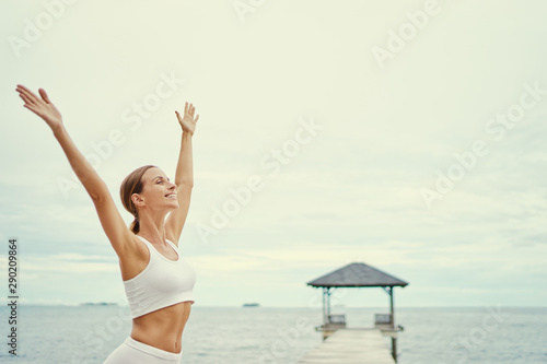 Victory and freedom. Enjoying the sea view. Morning yoga. Young woman raising hands up on the beach.