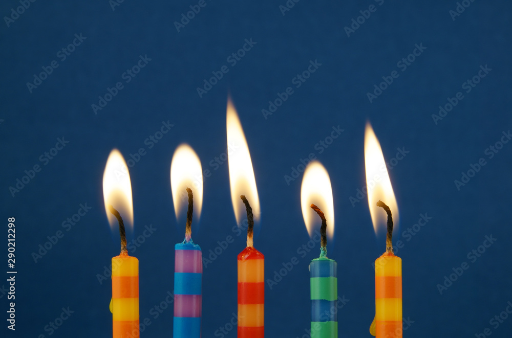 Colorful stripped birthday candles burning on blue background Colorful stripped birthday candles burning on blue background