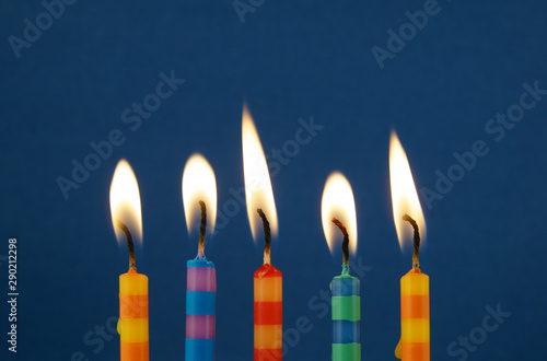 Colorful stripped birthday candles burning on blue background