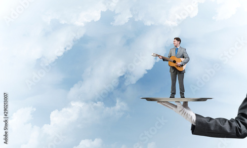 Businessman on metal tray playing acoustic guitar against blue sky background © adam121