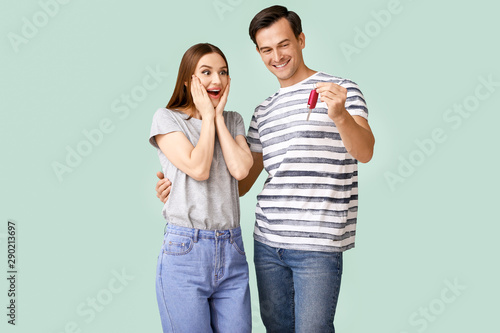 Happy couple with key from their new car on color background