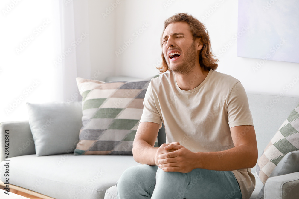 Young man suffering from pain in knee at home Young man suffering from pain in knee at home