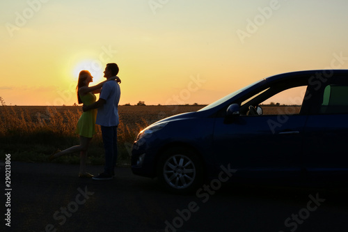 Silhouette of happy couple near their new car in countryside at sunset