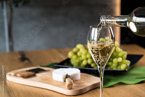 Pouring White wine with branches of grapes on a wooden table.