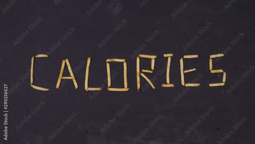 Obraz premium Word CALORIES laid out of long sticks of fried french fries on black background.