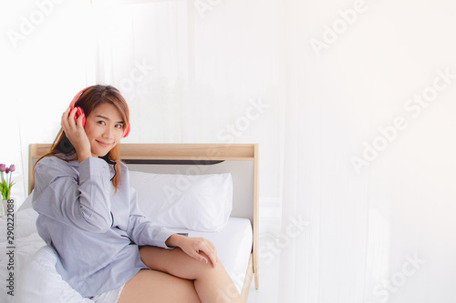Asian pretty female adult listen to music on headphone and sit on bed. Relax, enjoy and moden life style concept.