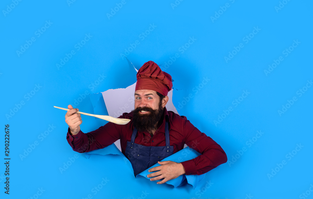 Bearded man chef preparing to cook food. Chief man in cook uniform with wooden spoon looking through paper. Bearded cook holds wooden kitchen cooking tools. Handsome chef cook with kitchen utensils. Bearded man chef preparing to cook food. Chief man in cook uniform with wooden spoon looking through paper. Bearded cook holds wooden kitchen cooking tools. Handsome chef cook with kitchen utensils.