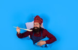 Bearded man chef preparing to cook food. Chief man in cook uniform with wooden spoon looking through paper. Bearded cook holds wooden kitchen cooking tools. Handsome chef cook with kitchen utensils.