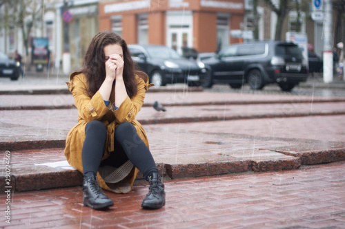 Sad young woman sitting outdoors in autumn on a rainy day.